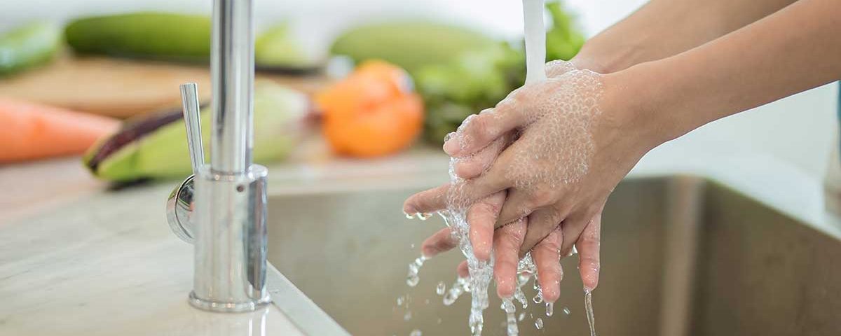 Lady washing hands near fruit.
