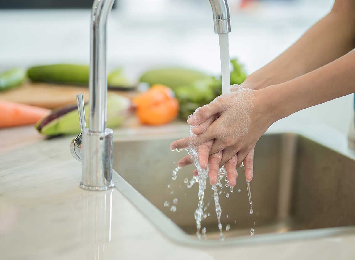 Lady washing hands near fruit.